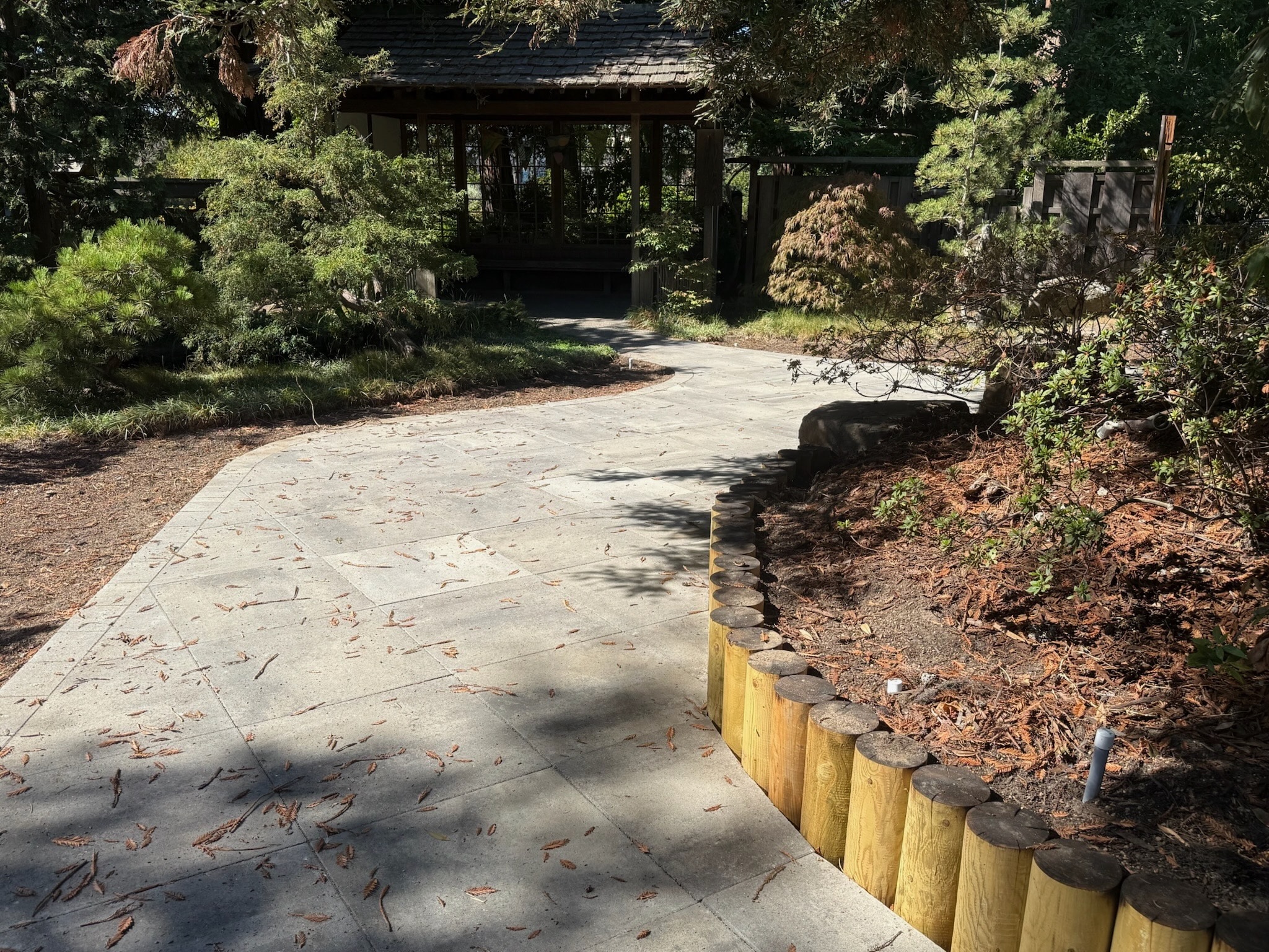 Curved paved path with defined borders runs through landscaped garden; includes existing structure suitable for potential renovation.
