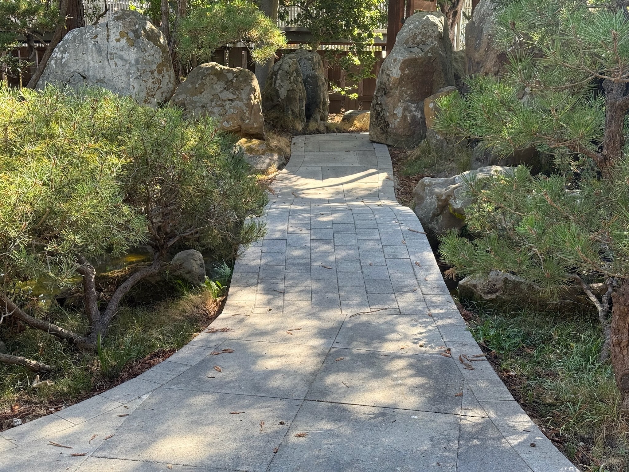 Curved stone pathway with established trees, rocks, and landscaping, offering potential for outdoor space enhancement and privacy.
