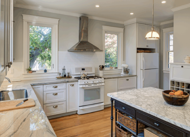 Renovated kitchen with updated cabinetry, stone countertops, premium appliances, gas stove, and ample daylight from dual windows.