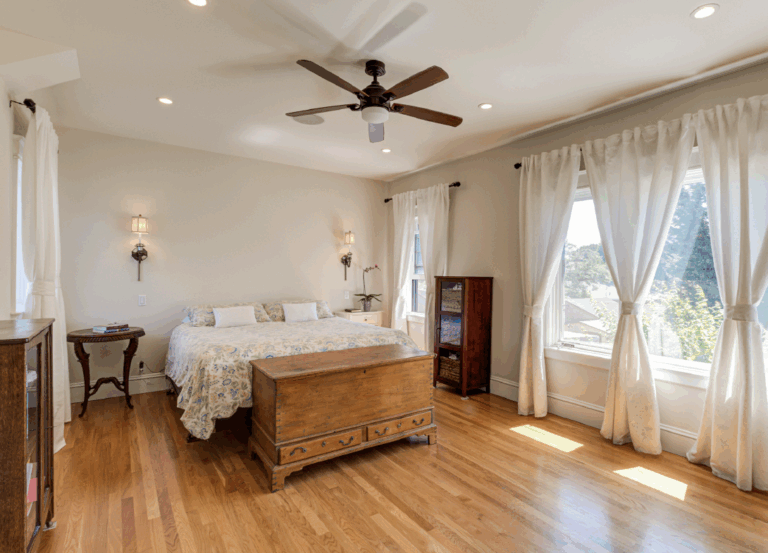 Bedroom features preserved hardwood floors, restored large windows for ample natural light, and ceiling fan for improved airflow.
