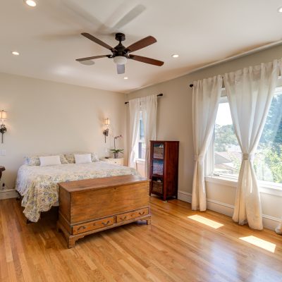 Alameda Addition bedroom with hardwood floors, ceiling fan, two windows for natural light, and sconce-ready wiring.