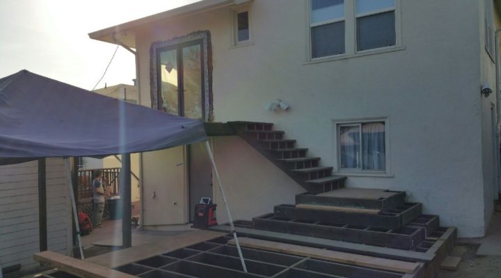 Two-story Rockridge home showing in-progress cascading deck and stair build; temporary canopy covers active construction zone.